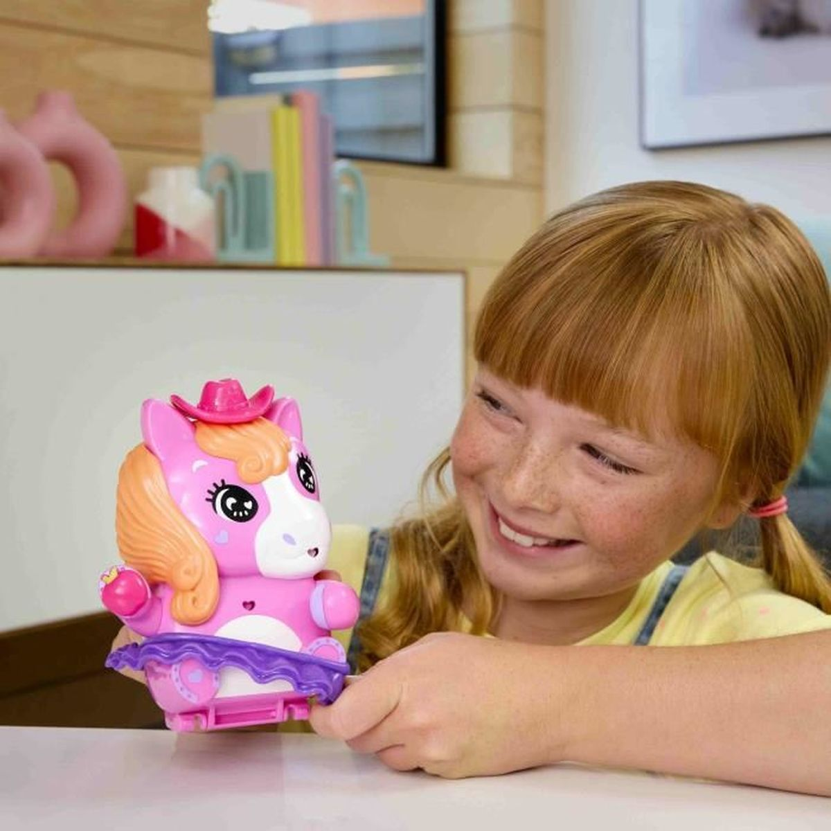 Ein Mädchen mit roten Haaren spielt mit einem rosa Spielzeugpferd mit Hut.
