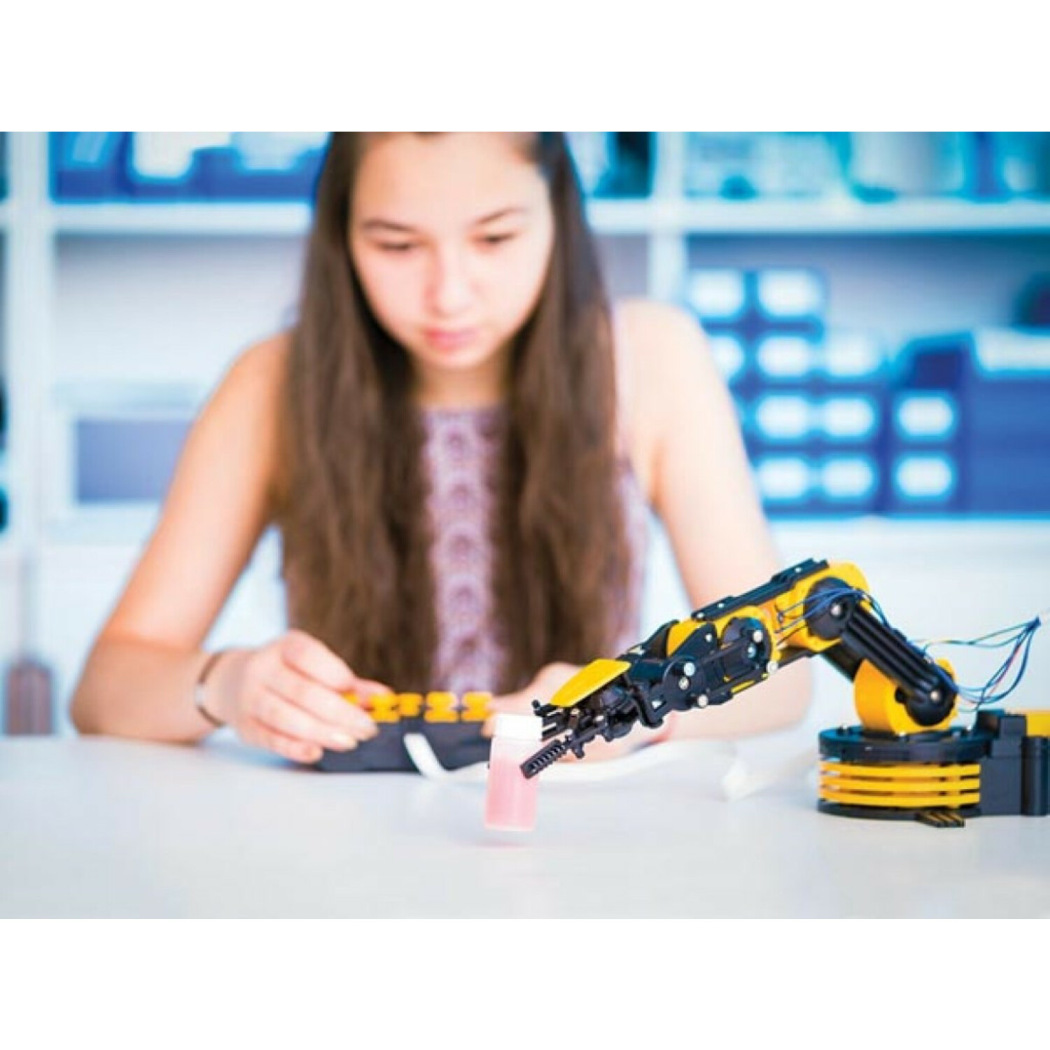 Una niña trabaja con un brazo robótico amarillo y un líquido rosa en un laboratorio.