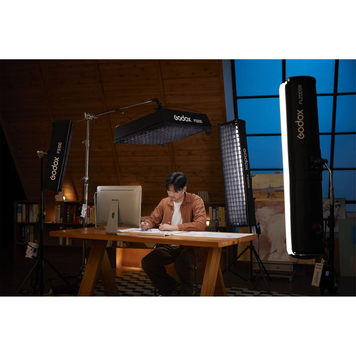 Mann sitzt am Schreibtisch, umgeben von Studiobeleuchtung.