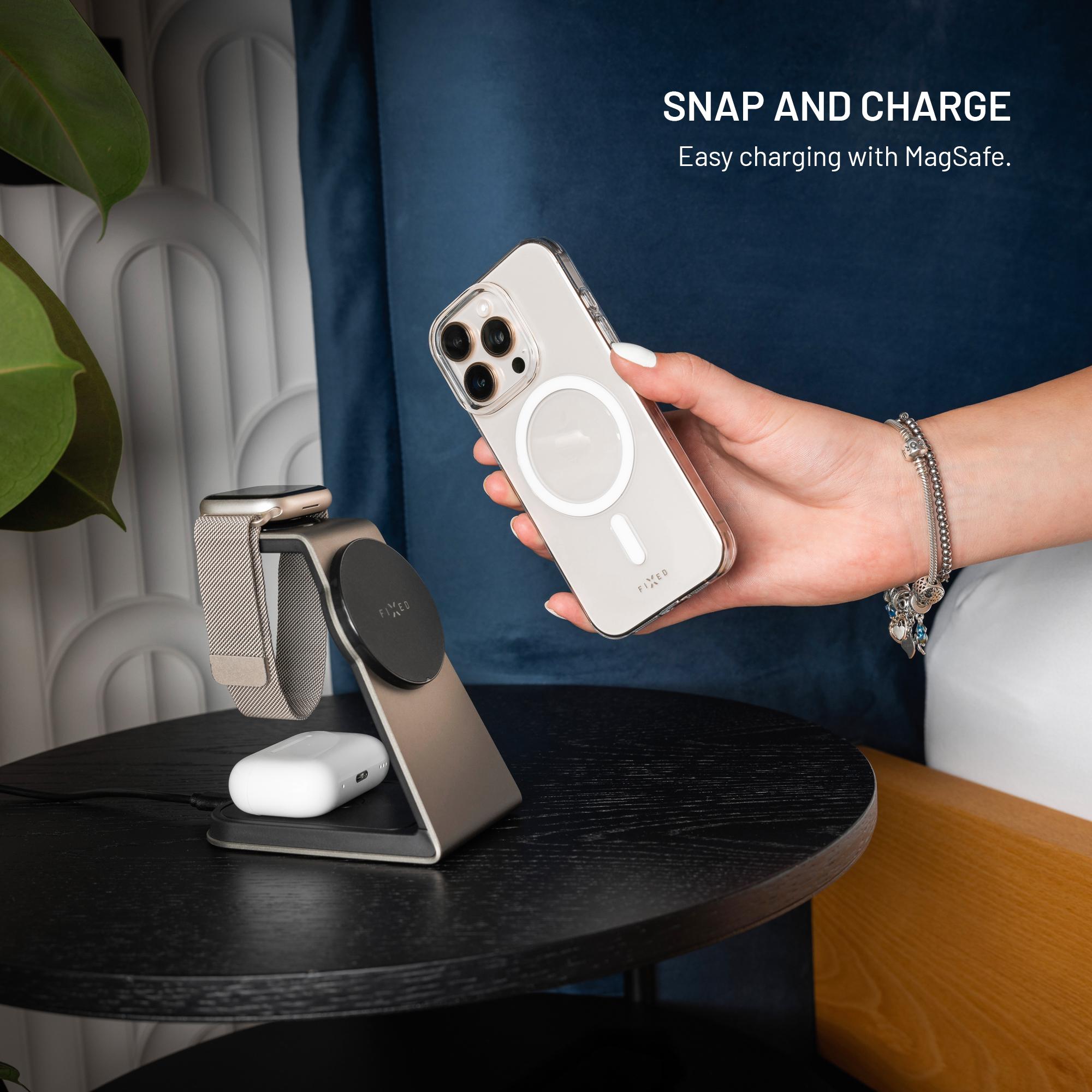 Ein Smartphone wird über MagSafe an eine Ladestation gehalten. Daneben sind eine Smartwatch und Ohrhörer.