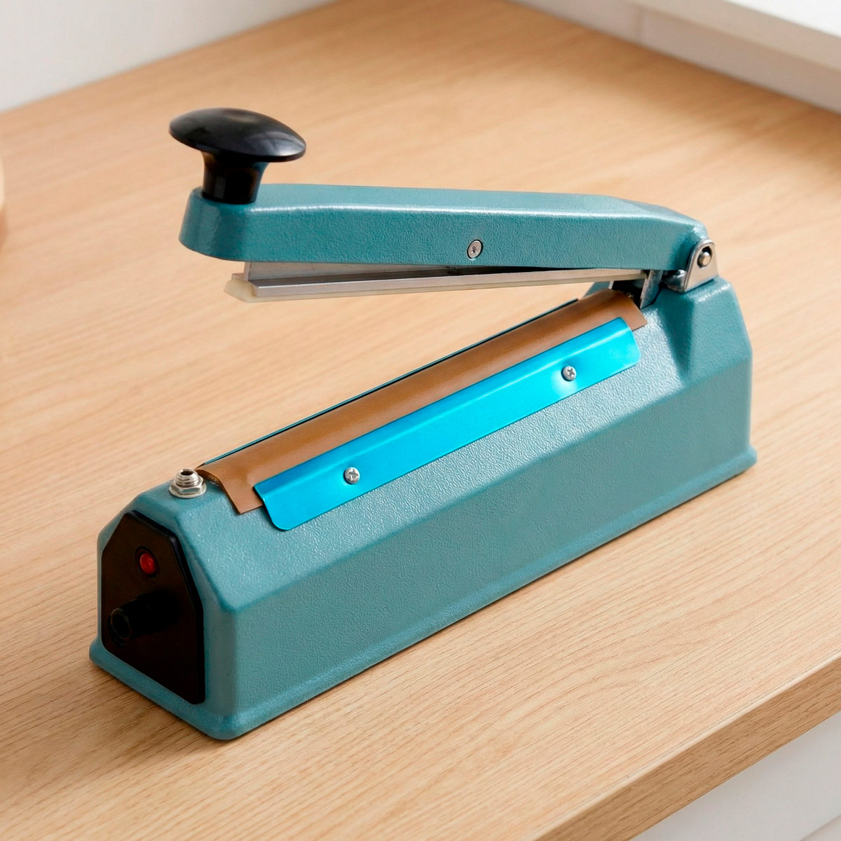 Türkise Siegelmaschine mit schwarzem Griff auf einem Holztisch.