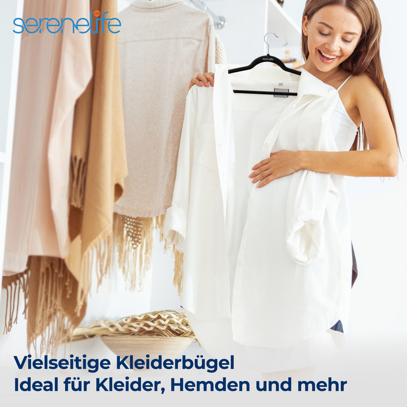 Eine Frau hält ein weißes Hemd vor Kleiderbügeln mit Kleidung. Sie lächelt.