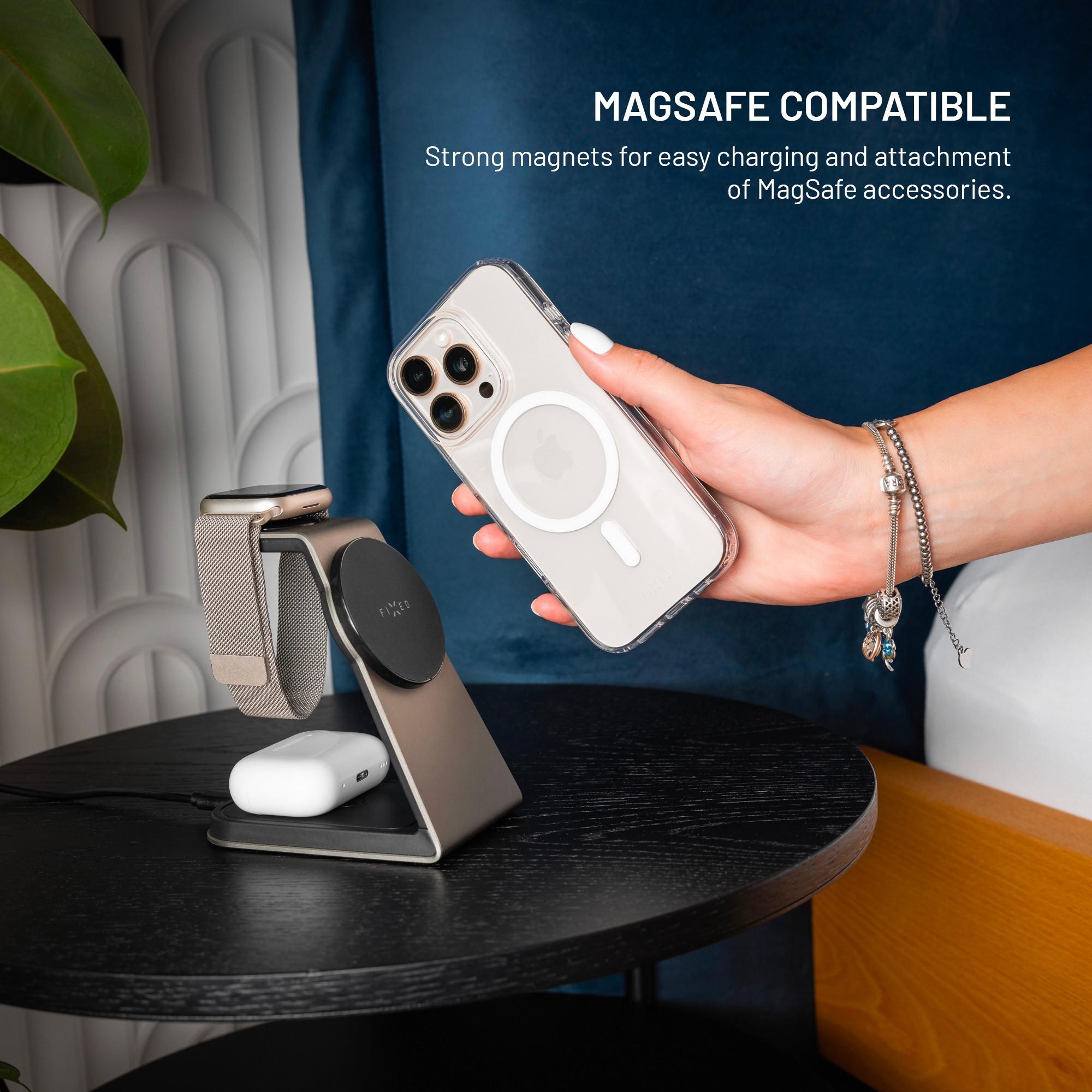 Eine Hand hält ein transparentes iPhone, daneben ein Ladeständer für Uhr und Kopfhörer.