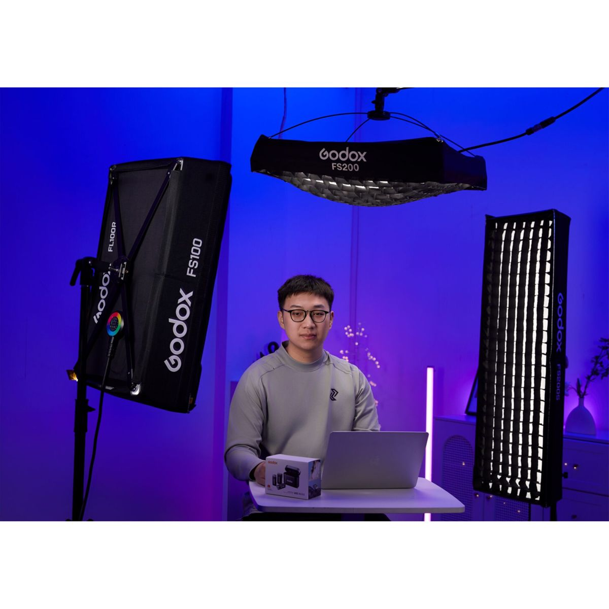 Ein Mann sitzt an einem Tisch mit einem Laptop, umgeben von Studiobeleuchtung.