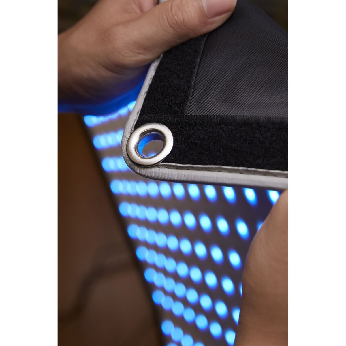 Hand mit Öse hält schwarzes Tuch mit blauen LEDs im Hintergrund.