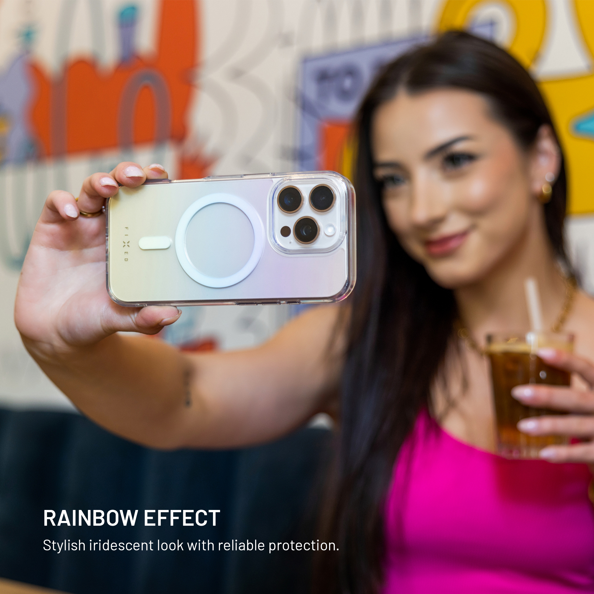 Frau hält Handy mit Regenbogeneffekt und trinkt Getränk. Bunte Wand.
