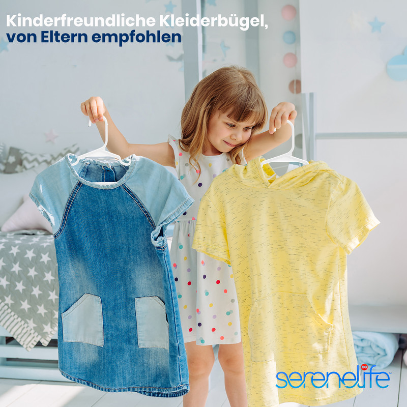 Ein kleines Mädchen hält zwei Kinderkleider auf Bügeln.