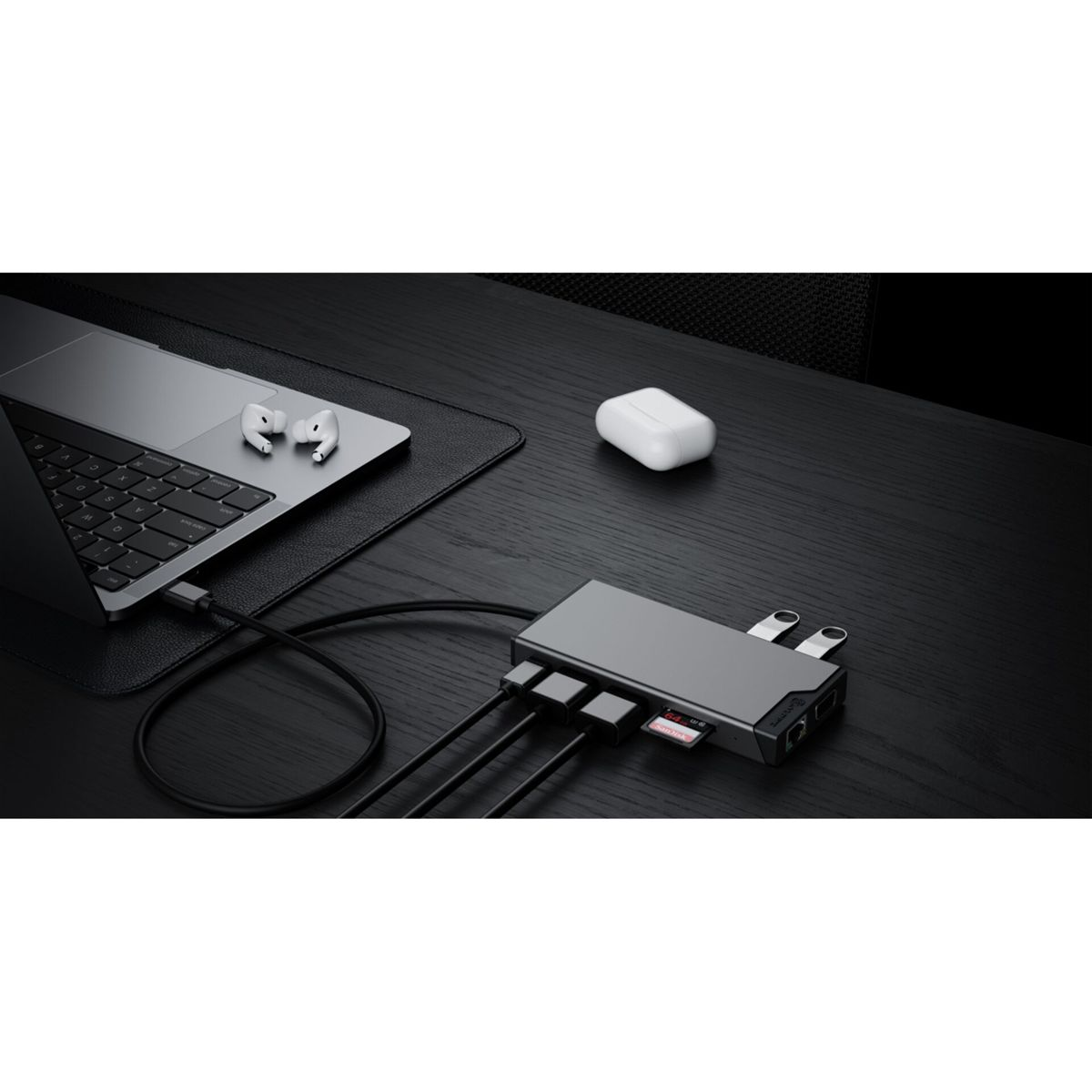Un ordinateur portable, des écouteurs et un étui de chargement blanc sont sur un bureau en bois foncé. Un hub USB-C gris avec des câbles se connecte à l'ordinateur portable.