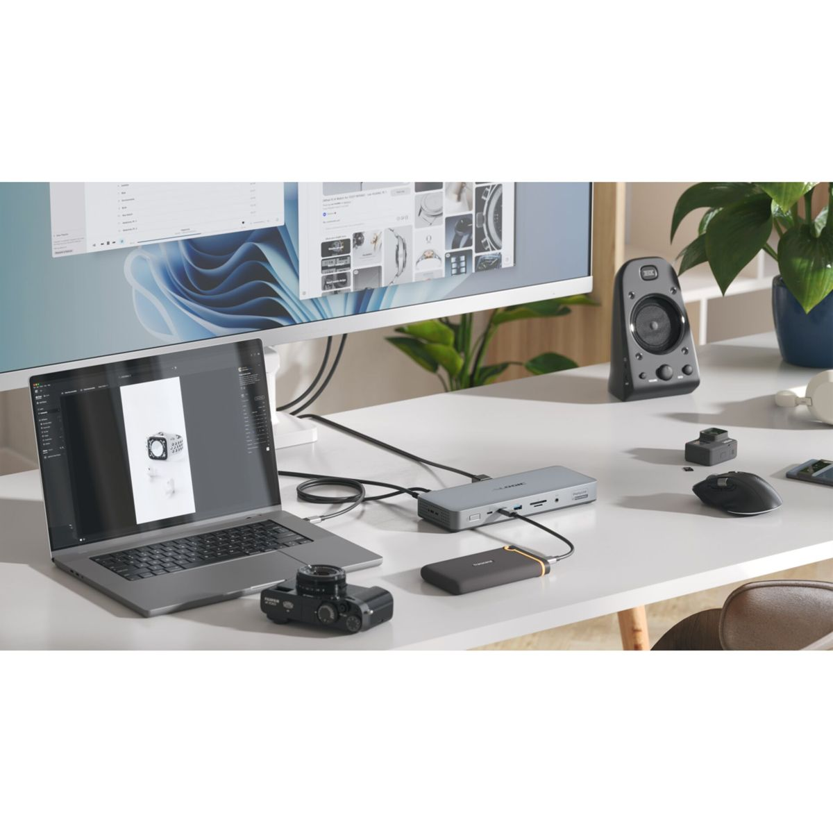 Ein Schreibtisch mit Laptop, externer Festplatte, Dockingstation, Kamera, Maus und Lautsprecher.