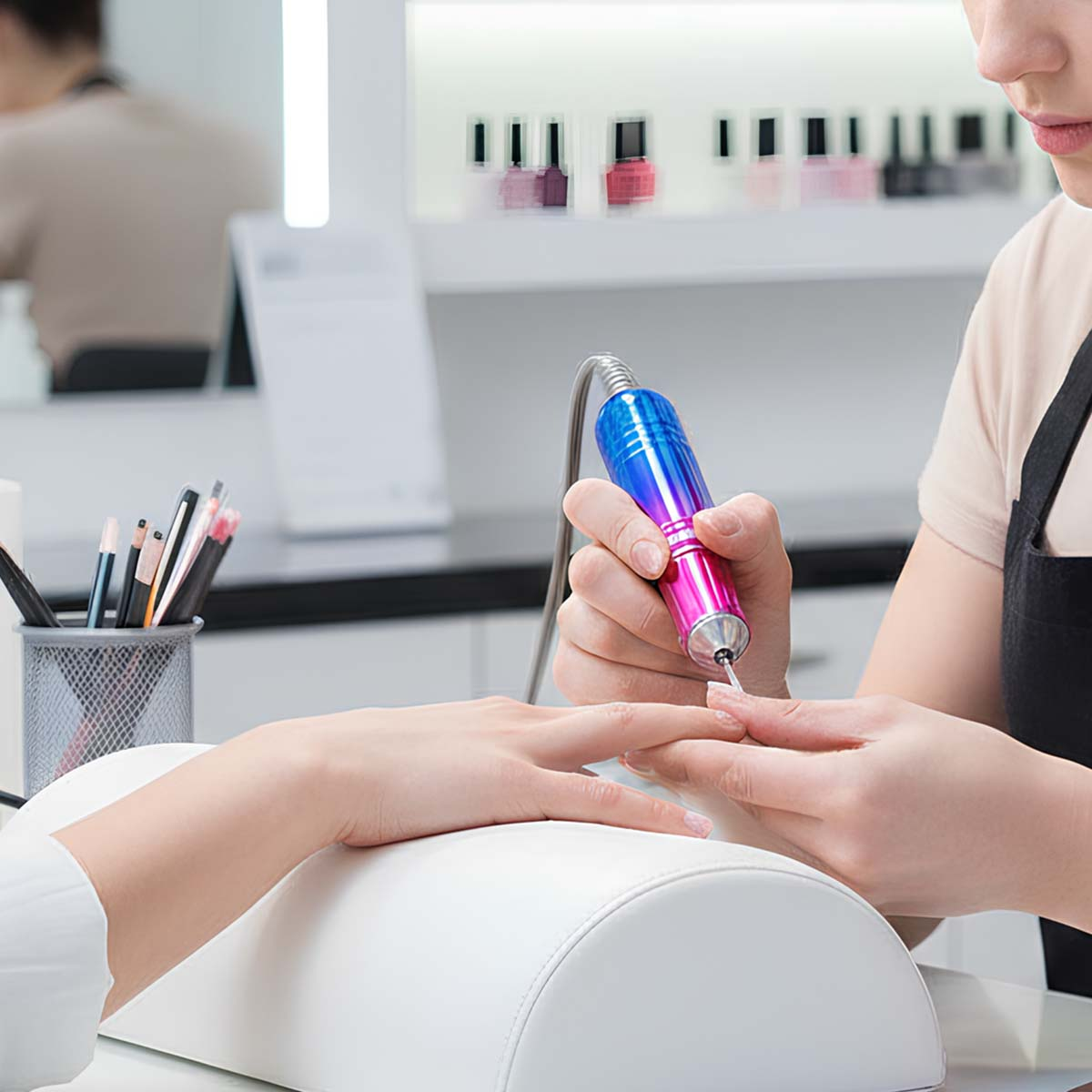 Ein Nageldesigner bearbeitet mit einem elektrischen Nagelfräser den Nagel einer Kundin.