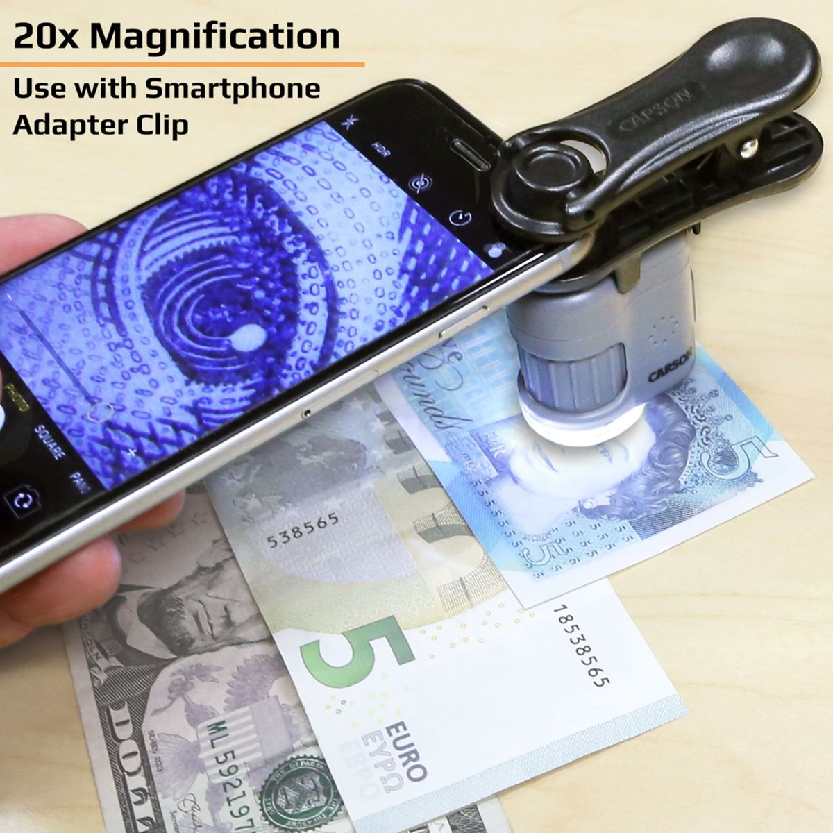 Smartphone mit 20-fachem Vergrößerungsclip betrachtet Euro- und Dollarnoten auf Holzoberfläche.