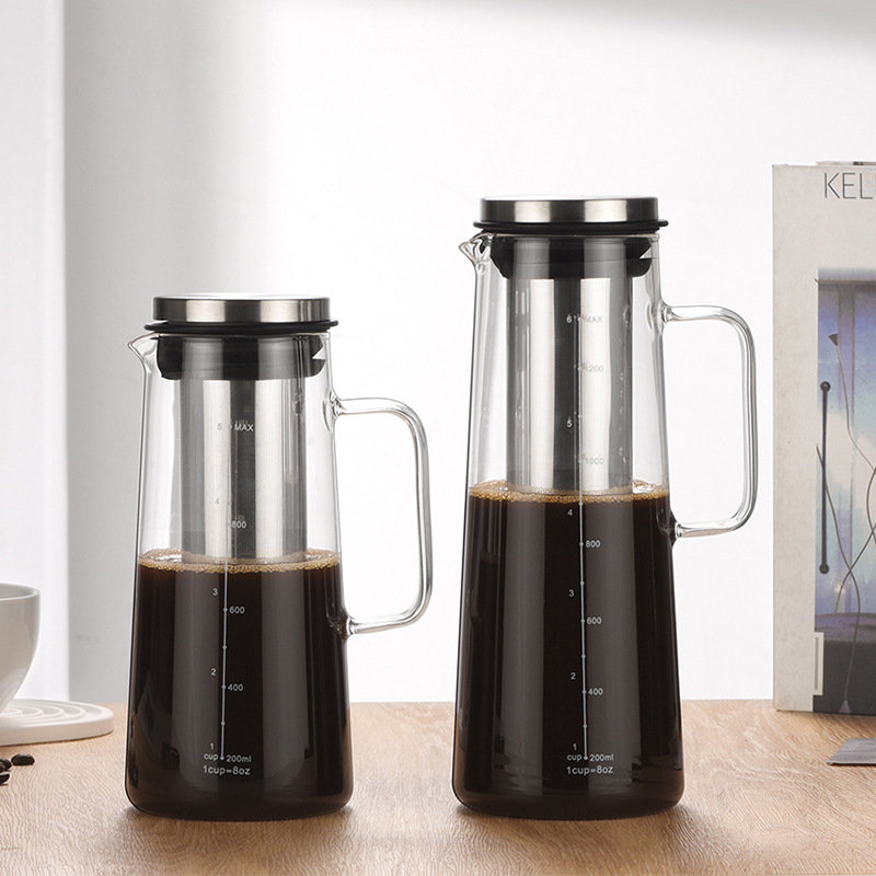 Zwei Glas-Kaltkaffeebereiter mit Metalleinsätzen und Deckeln auf Holzoberfläche.
