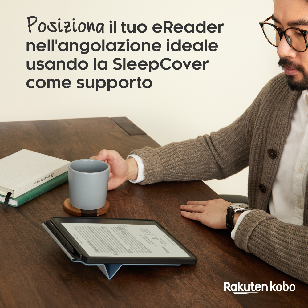 Uomo con occhiali tiene una tazza su un tavolo di legno accanto a un e-reader.