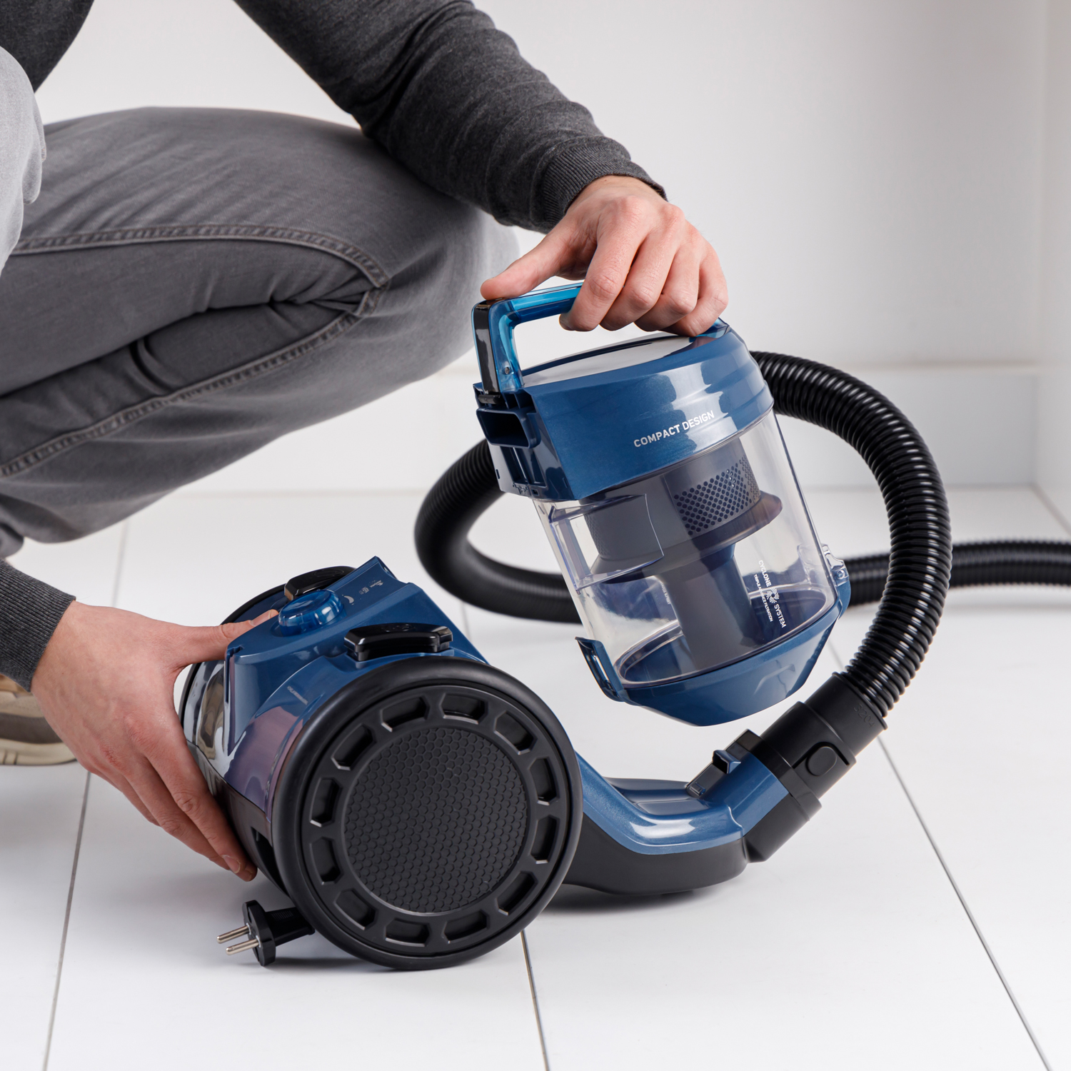 Una persona tiene un contenitore per aspirapolvere blu collegato a un tubo.