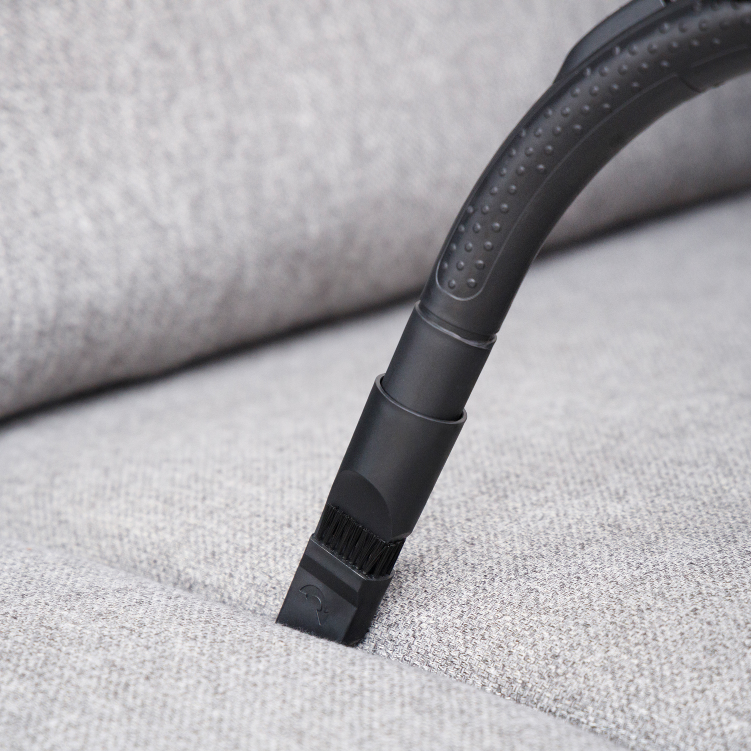 Un accessorio per aspirapolvere nero pulisce un rivestimento in tessuto grigio chiaro.