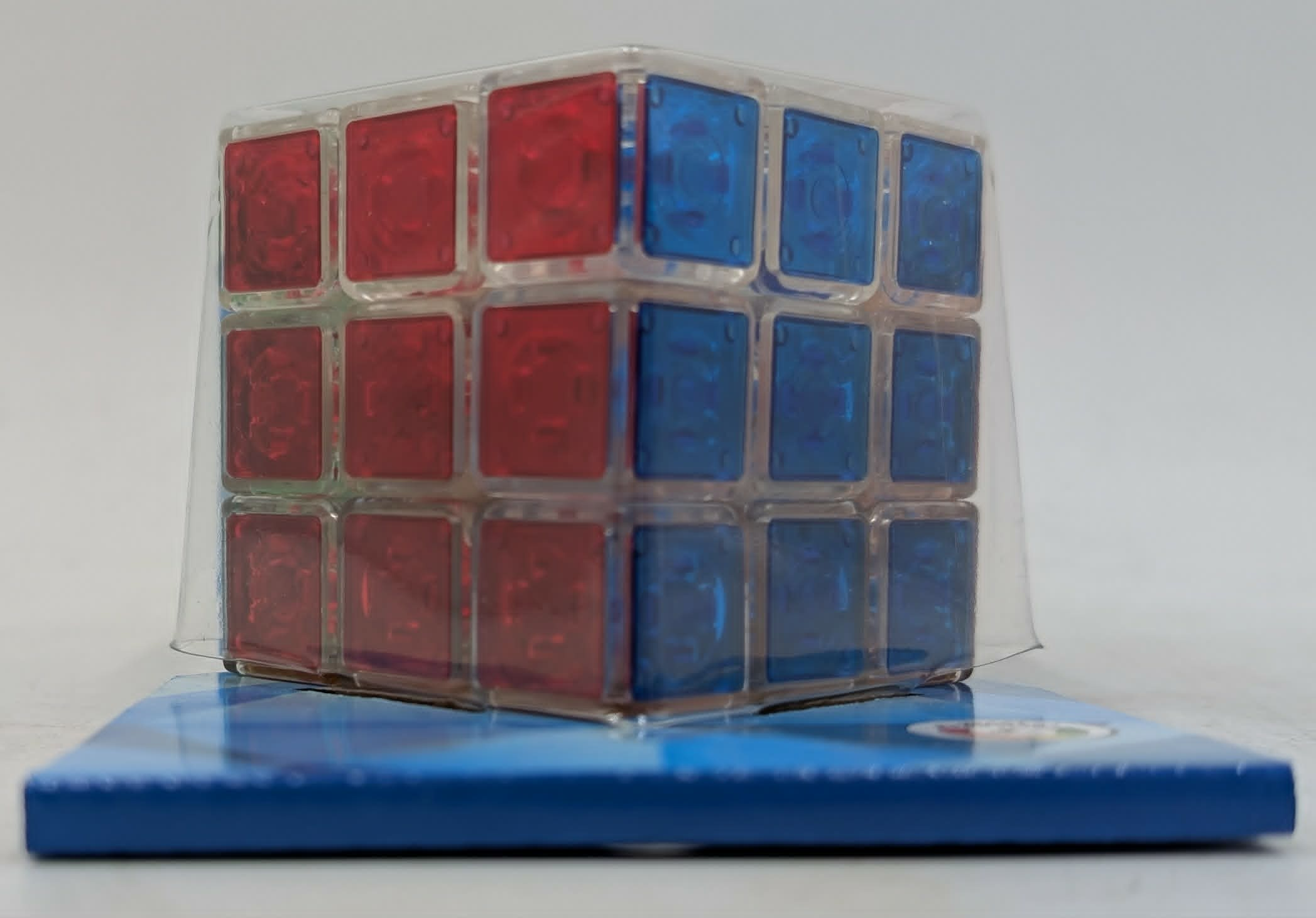 Ein transparenter Würfel mit roten und blauen Feldern liegt auf einer blauen Unterlage.