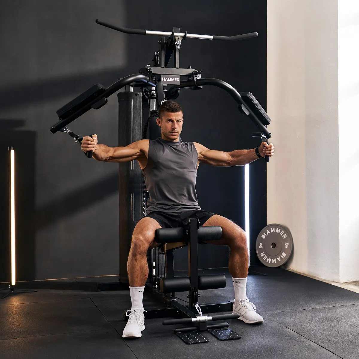 Mann trainiert mit Fitnessgerät im Fitnessstudio, dunkler Hintergrund, Lichter.