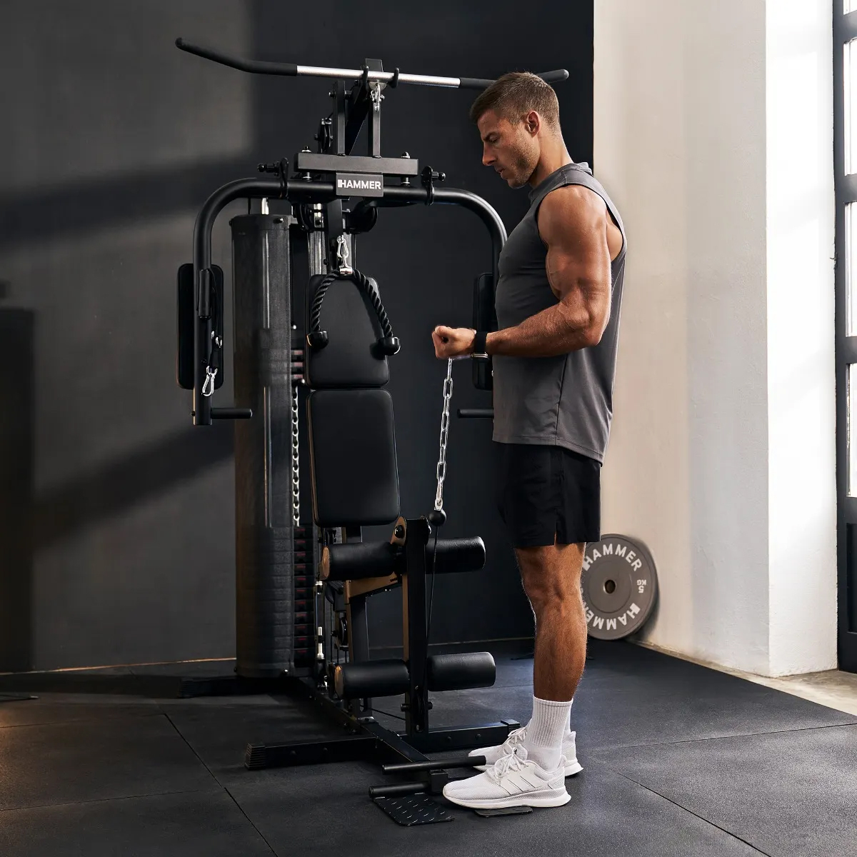 Mann mit muskulösen Armen trainiert Bizeps an einer schwarzen Hantelbank im Fitnessstudio.