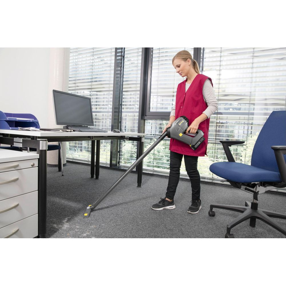Una donna aspira il tappeto in un ufficio con un aspirapolvere portatile.