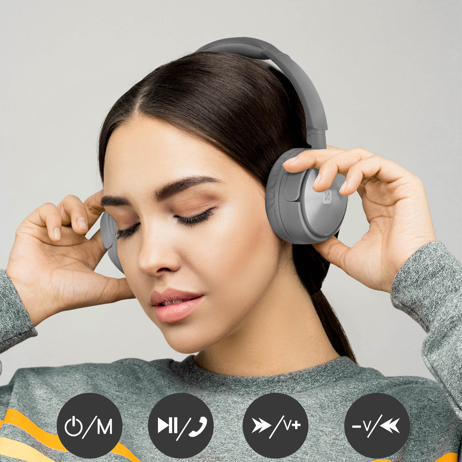 A woman wearing grey headphones, holding them with both hands.