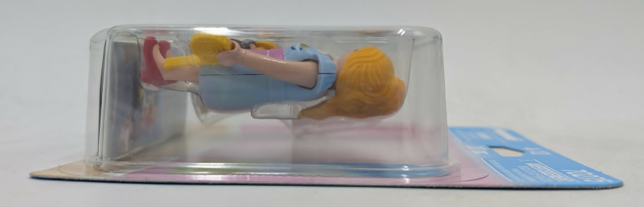 Una bambola in abiti blu con capelli biondi giace nella confezione.