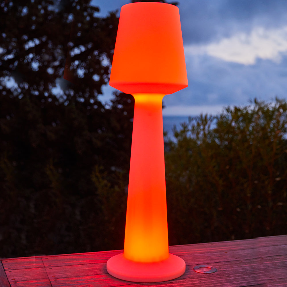 Eine leuchtende orangefarbene Stehleuchte steht auf einer Holzterrasse bei Dämmerung.