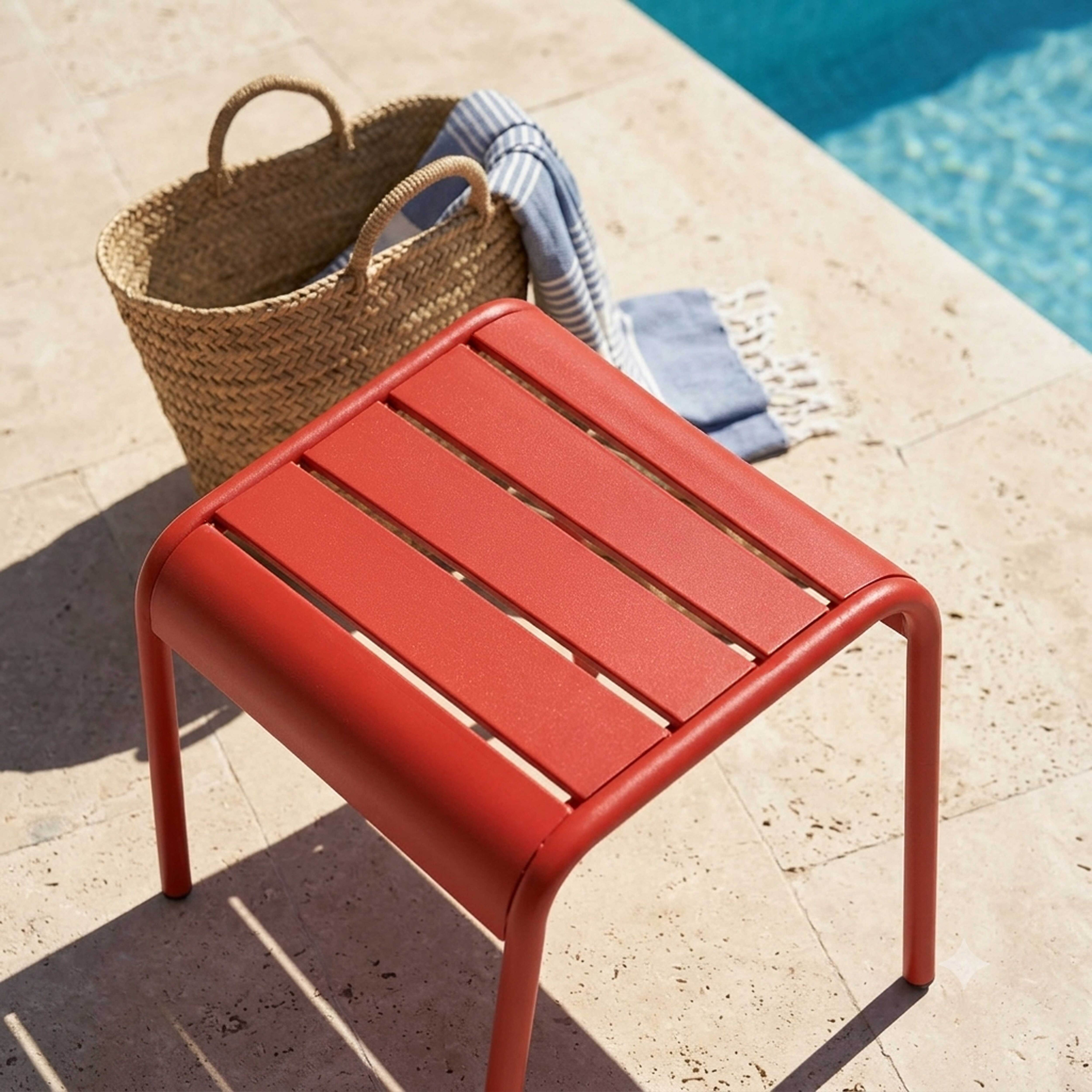 Ein roter Hocker neben einem geflochtenen Korb mit Handtuch am Pool.