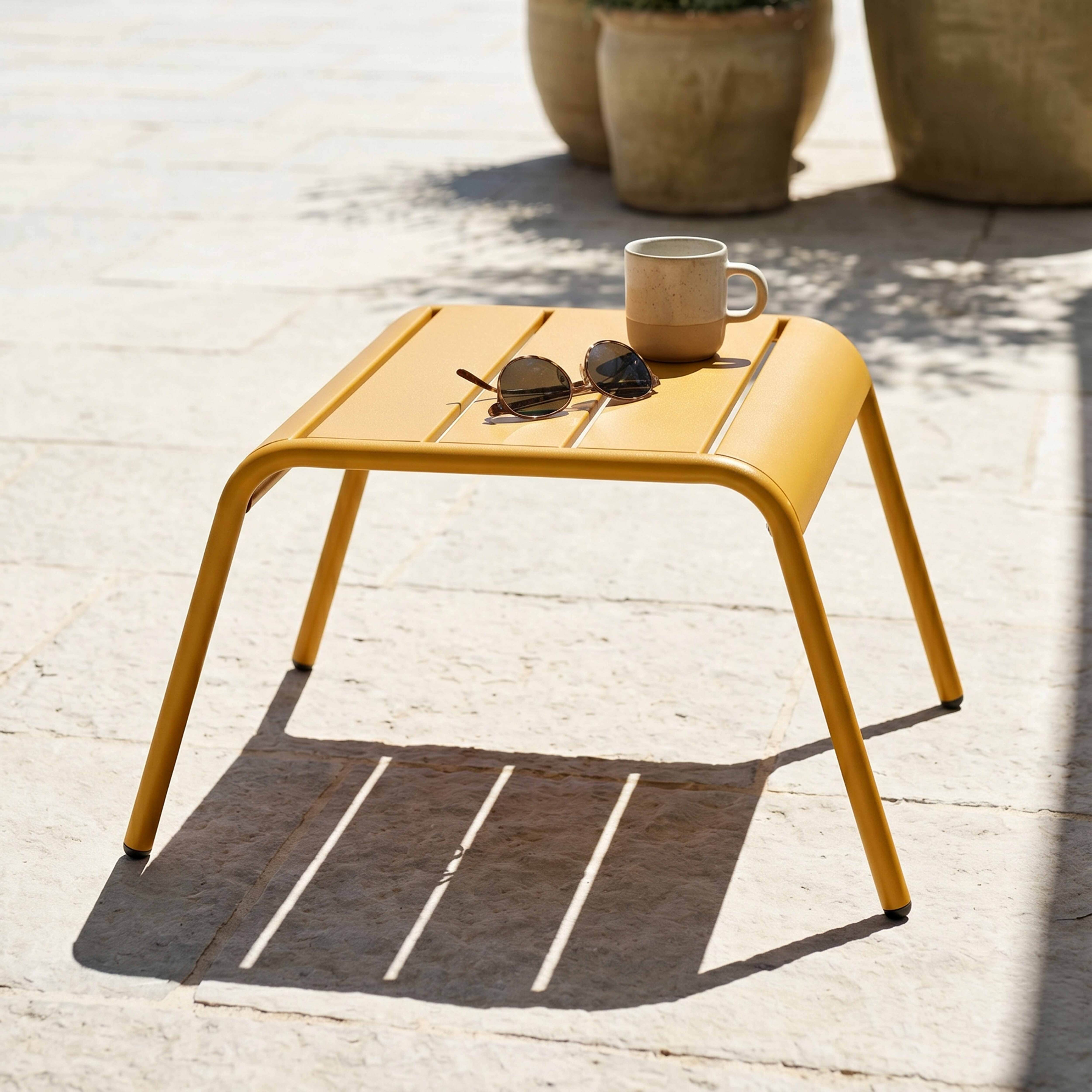 Ein gelber Beistelltisch mit Sonnenbrille und Tasse im Freien.