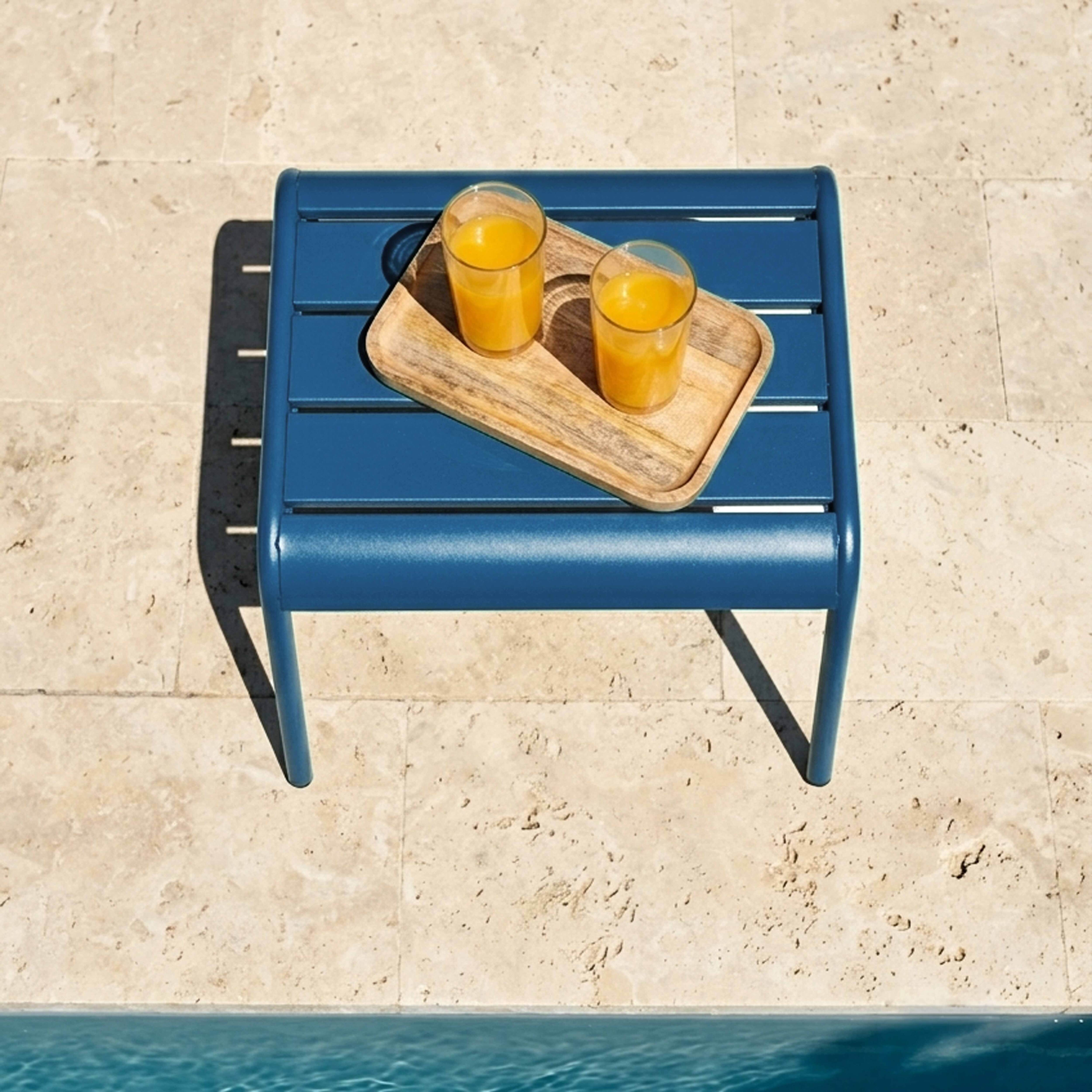 Blaue Liege mit zwei Gläsern Saft auf Holzteller, nah am Pool.