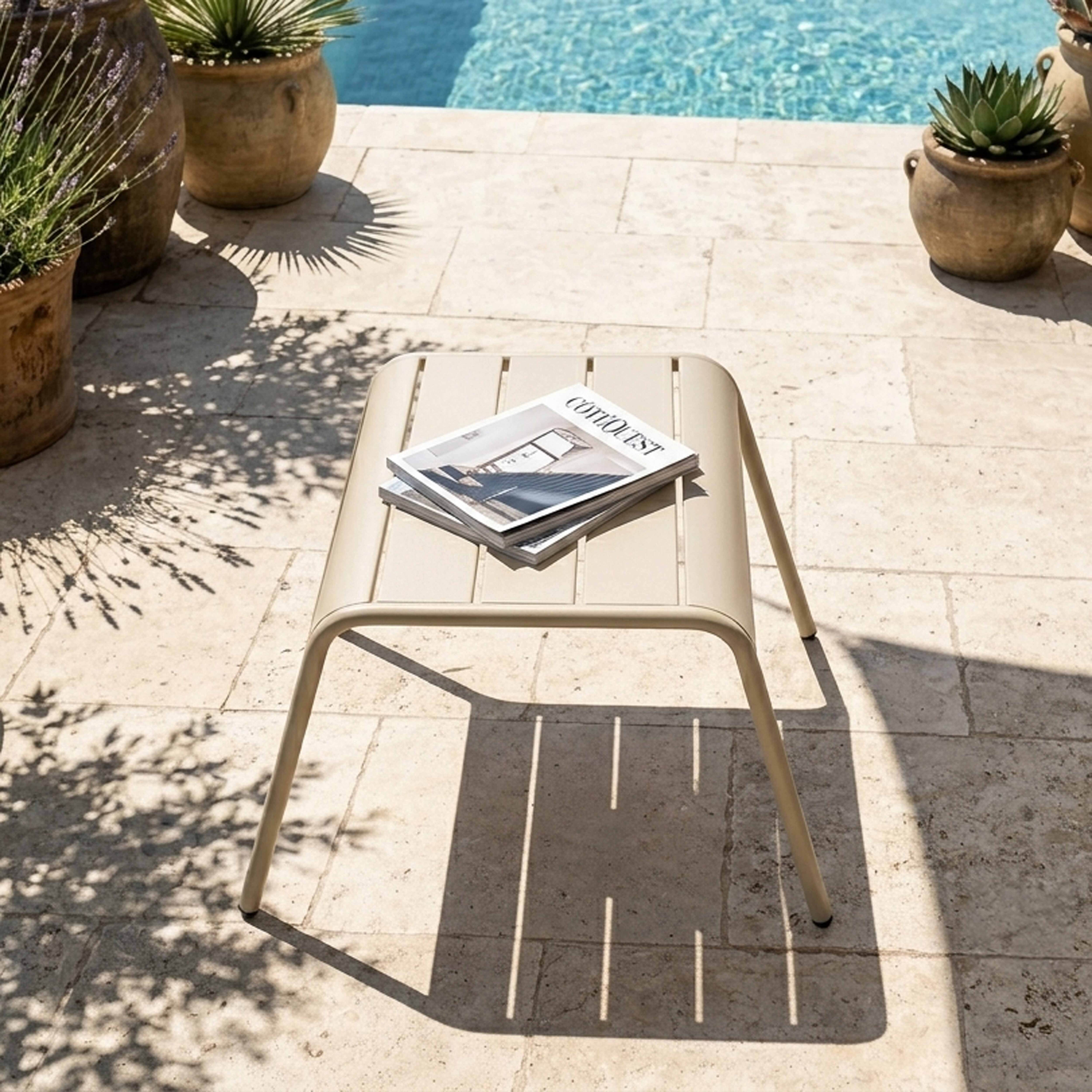 Ein beiger Tisch mit Magazinen steht auf einer gefliesten Terrasse neben einem Pool.