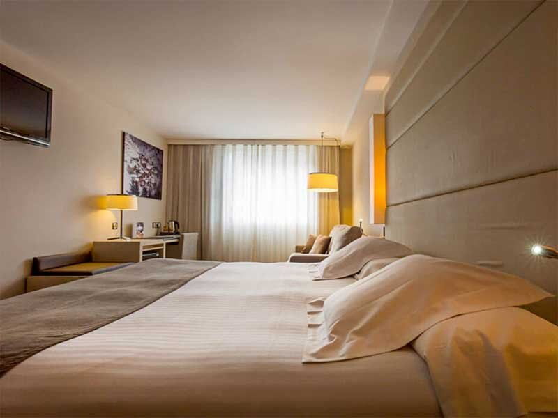 Una habitación de hotel con una cama grande, escritorio, TV y lámparas.