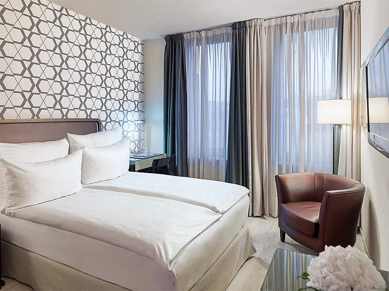 Habitación de hotel con dos camas, sillón y escritorio.