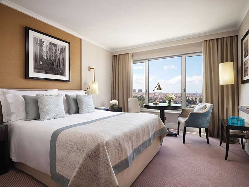 Una habitación de hotel con una cama grande, una mesa junto a la ventana con vistas a la ciudad y un sillón.