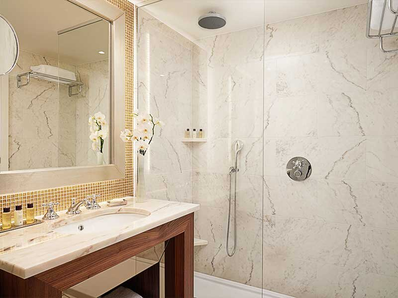 Baño moderno con azulejos de mármol, lavabo y cabina de ducha separada.