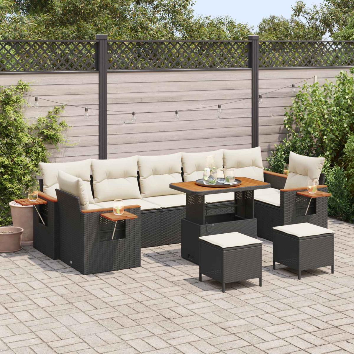 Dunkelgraue Rattan-Lounge-Möbel mit cremefarbenen Kissen, ein Tisch und Hocker auf einer Pflasterterrasse.