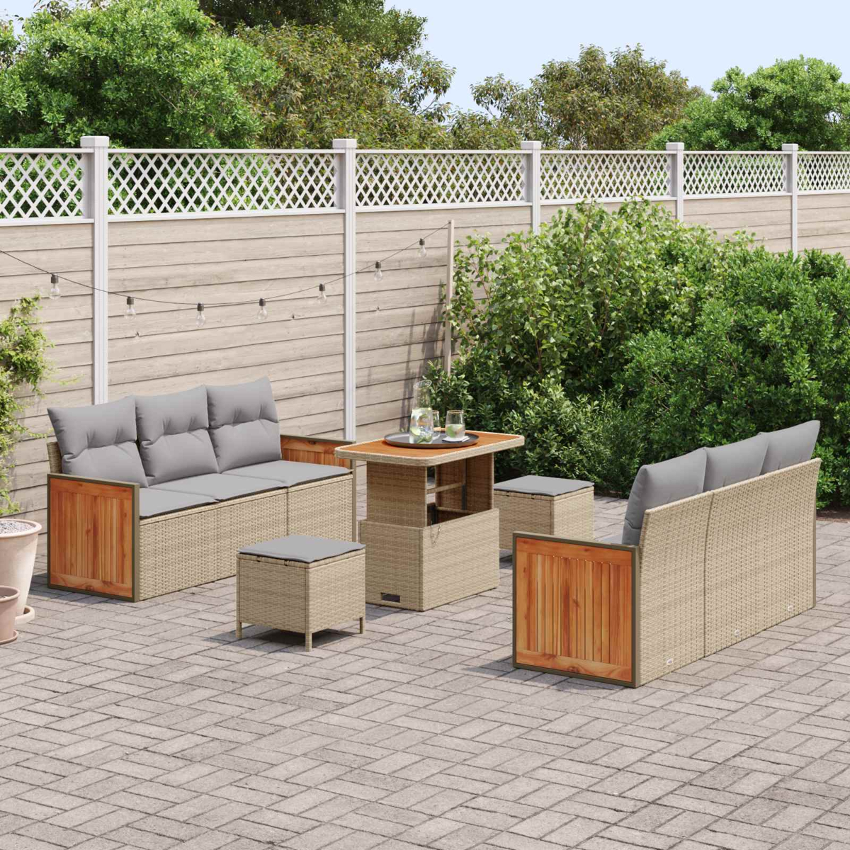 Ein Gartenmöbel-Set aus Rattan mit grauen Kissen auf einer gepflasterten Terrasse.