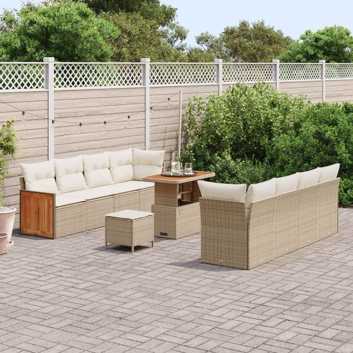 Un set di divani in rattan beige con cuscini chiari su un patio pavimentato con recinzione.