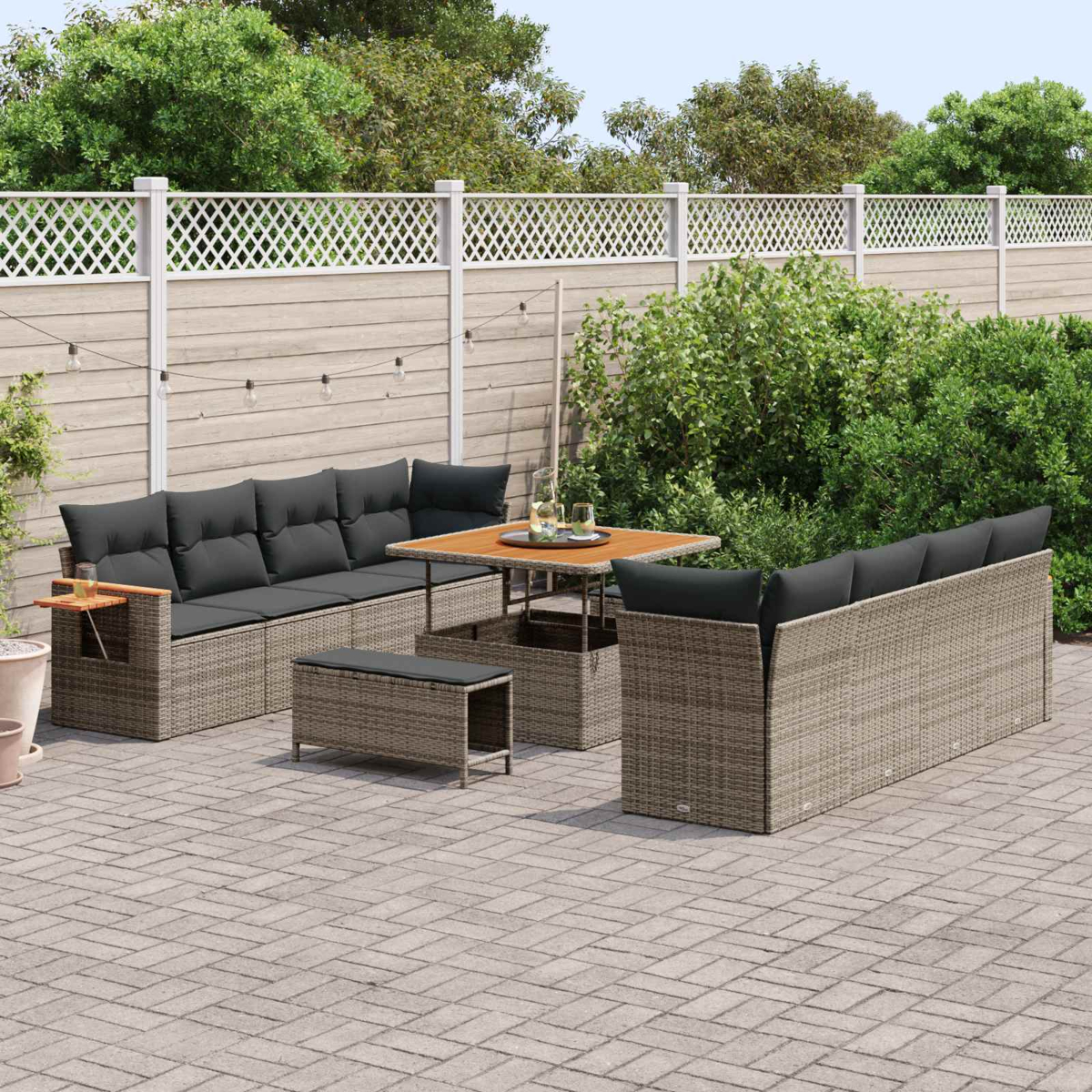 Geflochtene Gartenmöbel mit grauen Kissen auf einer Kopfsteinpflasterterrasse.