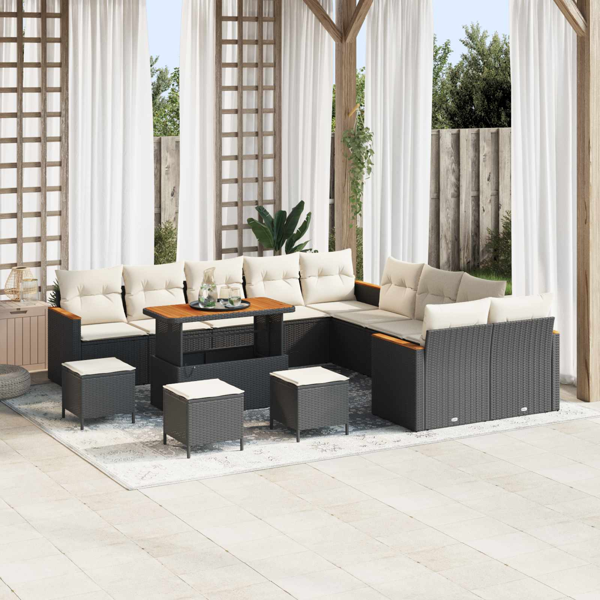 Ein dunkles Rattan-Sofa mit hellen Kissen und Hockern steht auf einer Terrasse.