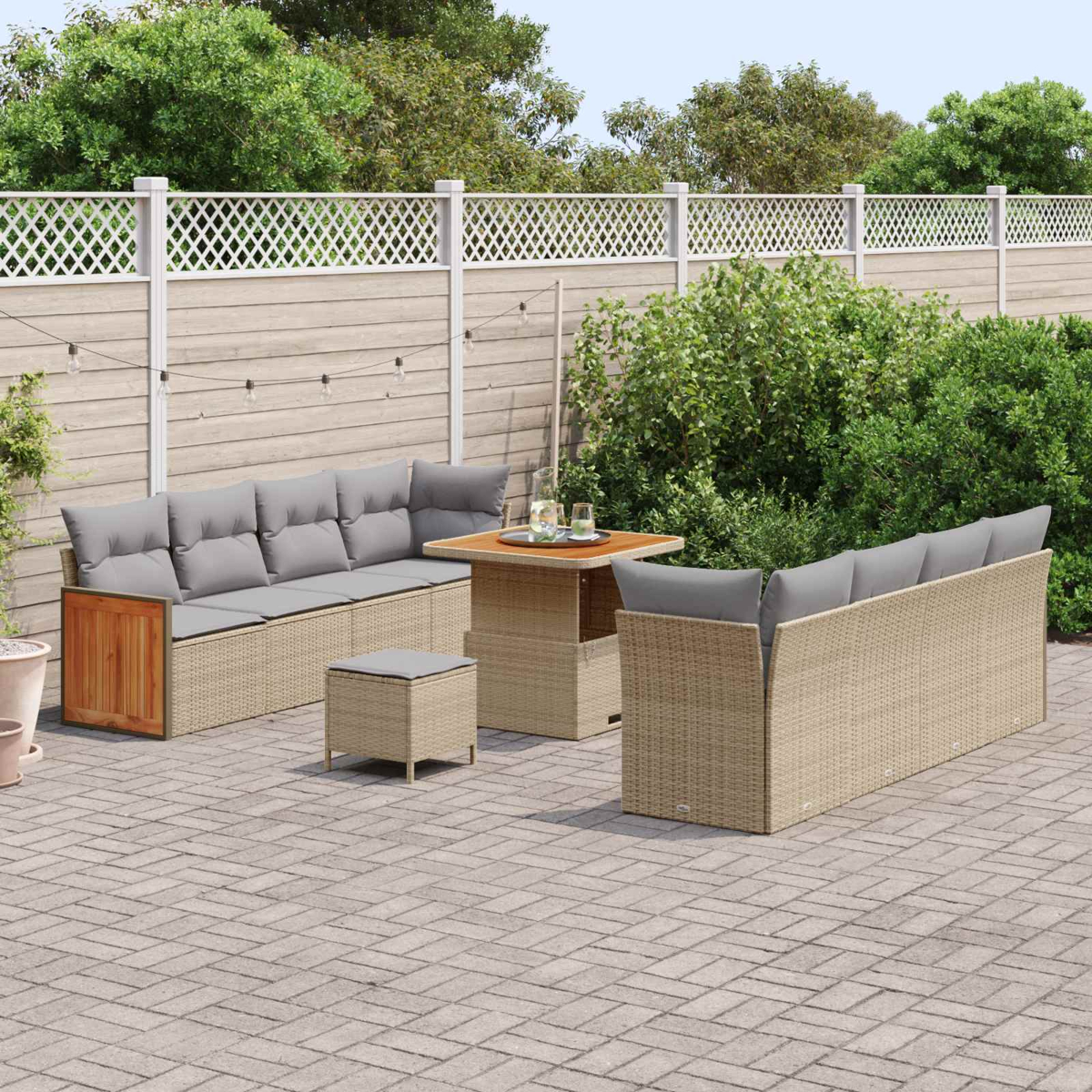Gartenlounge mit beigefarbener Rattan-Eckcouch, Tisch und Hocker auf Kopfsteinpflaster.