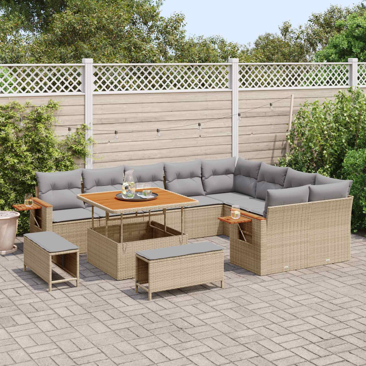 Ein beiger Rattansofa-Set mit grauen Kissen steht auf einer gepflasterten Terrasse.