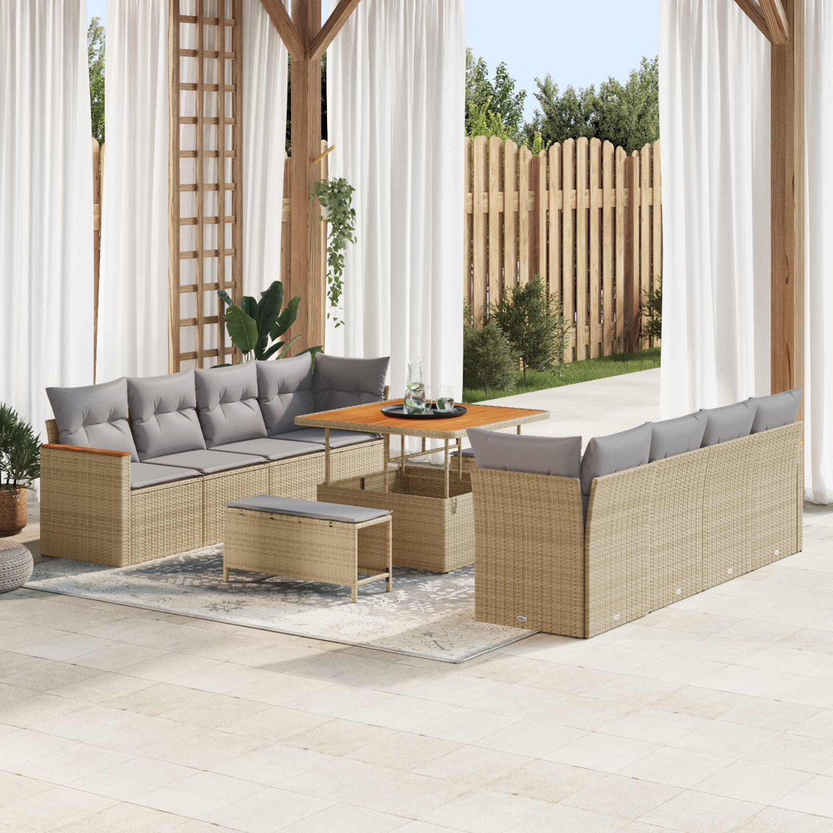 Ein Gartenlounge-Set aus Rattan mit grauen Kissen, Tisch und Bank vor einem Holzzaun.