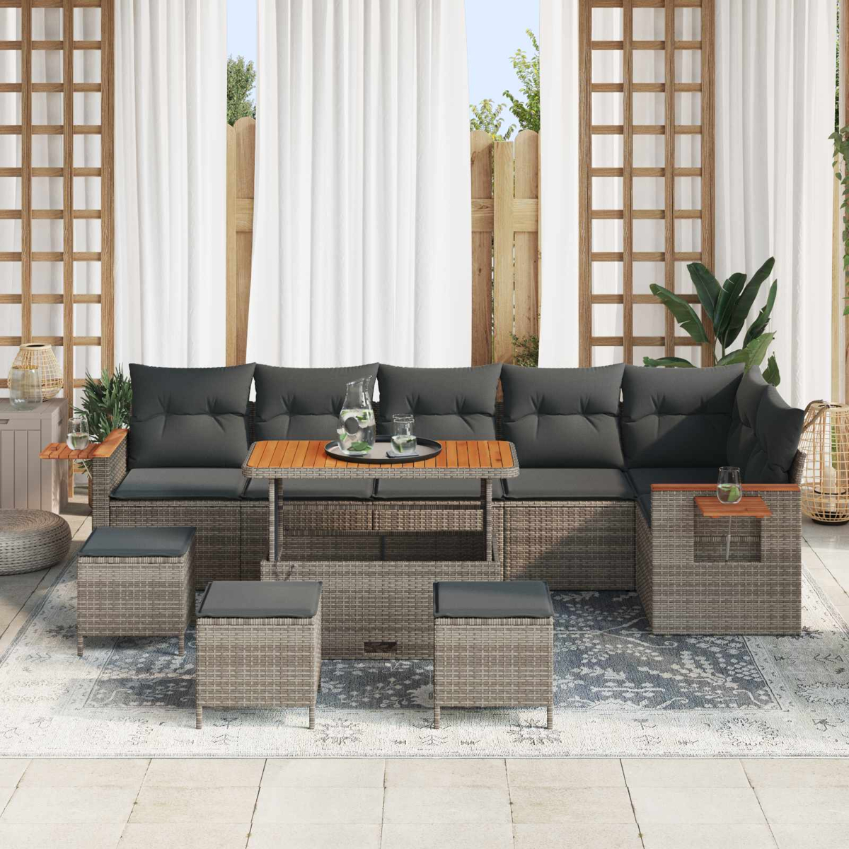 Graues Rattan-Ecksofa mit dunklen Kissen, Holztisch und Hockern auf einem Teppich.
