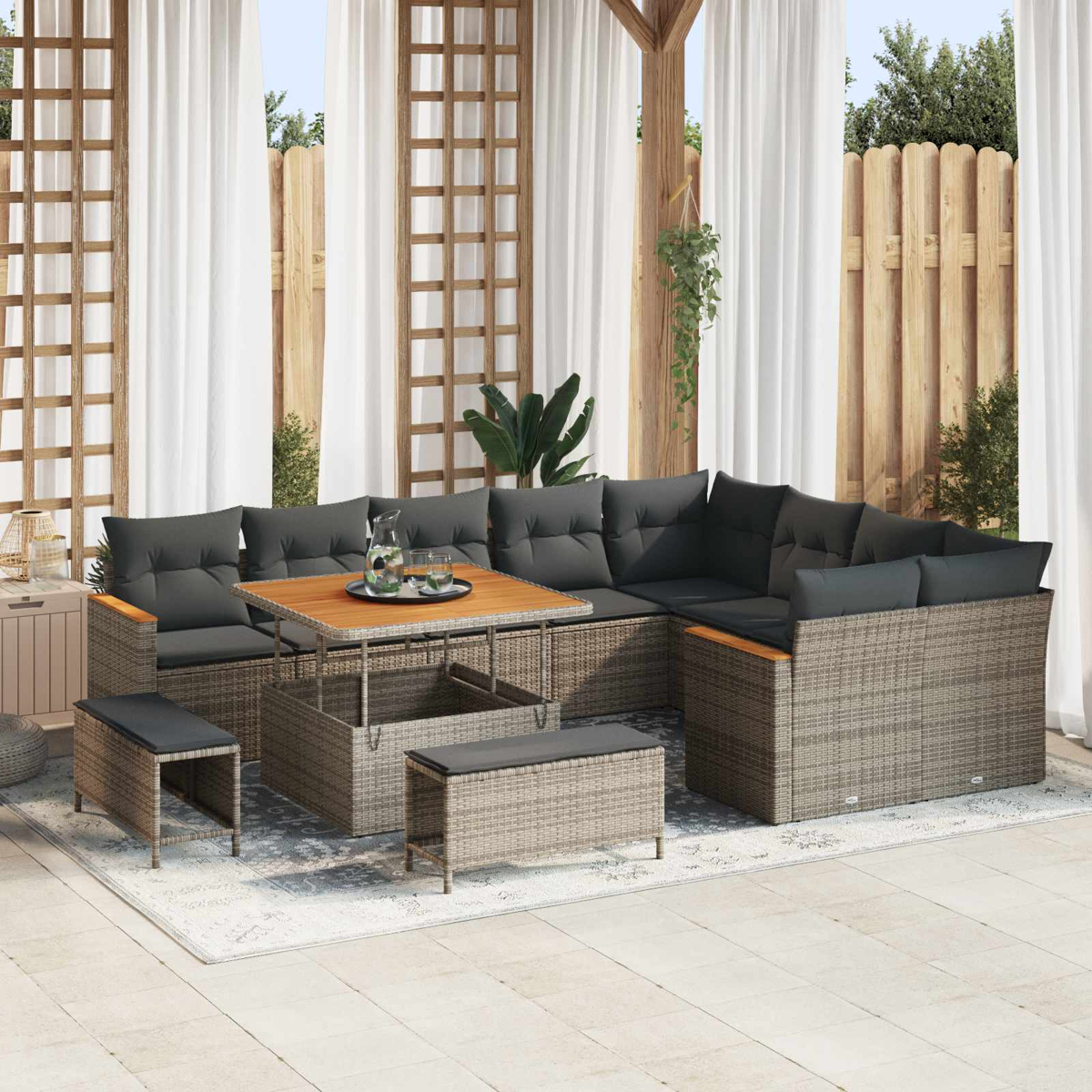 Un sofá gris de mimbre con mesa y taburetes en un patio bajo cortinas blancas.