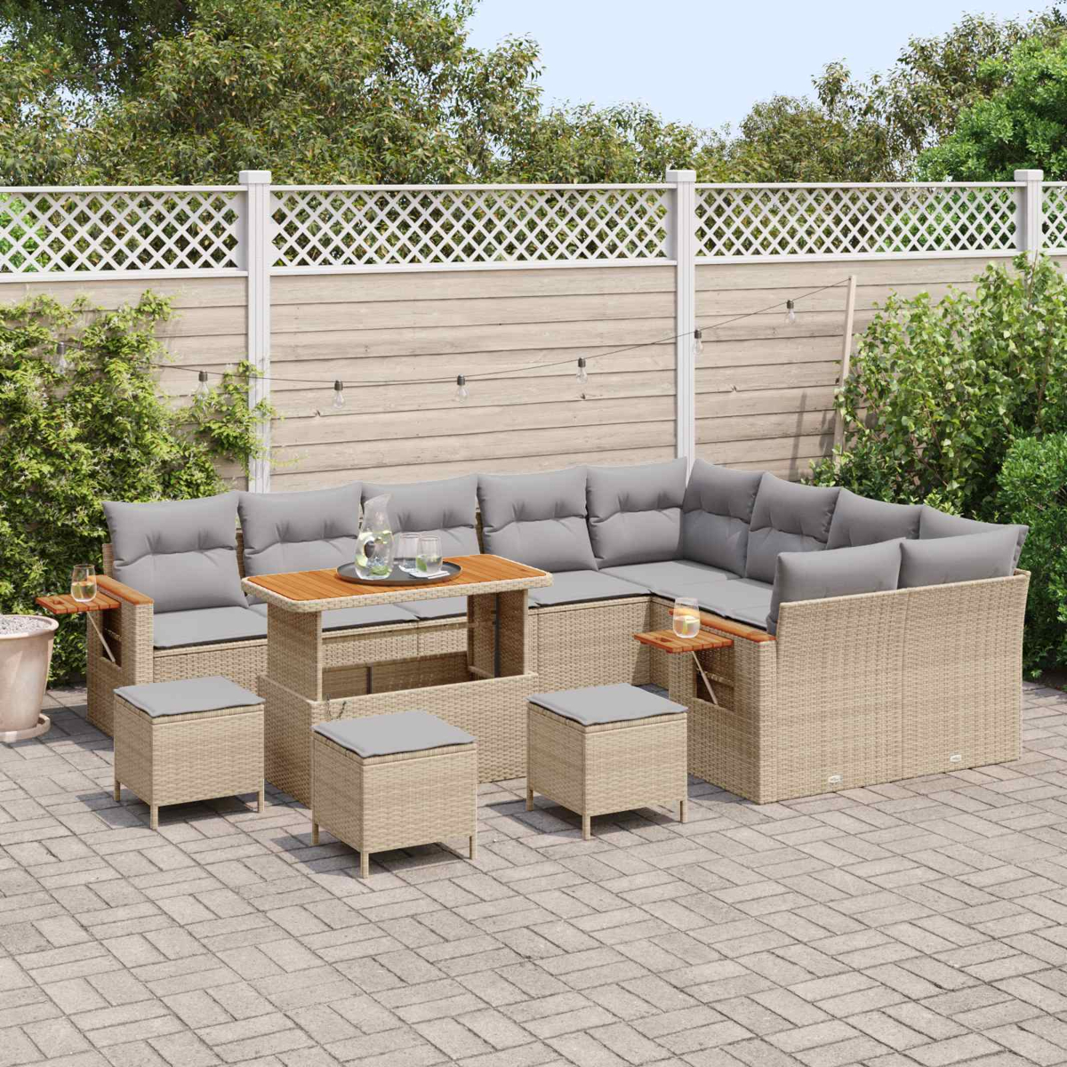 Geflochtenes Gartenmöbel-Set mit grauen Kissen und Holztisch auf einer gepflasterten Terrasse.