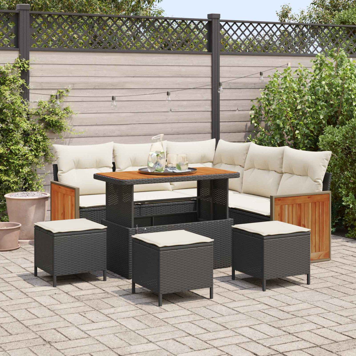 Ein Gartenmöbelset aus Rattan mit cremefarbenen Kissen und Hockern auf einer Steinpflasterung.