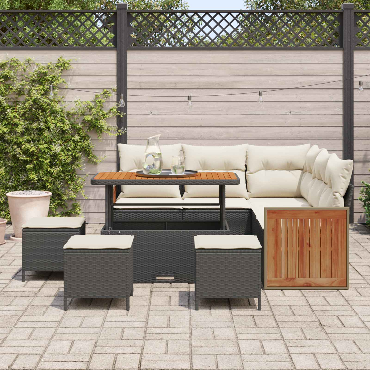 Ein Gartenmöbel-Set mit Sofa, Tisch und Hockern auf einer gepflasterten Terrasse.