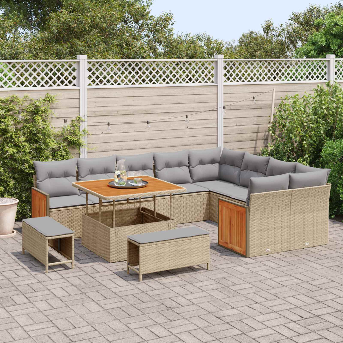 Ein rattanartiges Lounge-Set mit grauen Kissen und einem Holztisch auf einer Kopfsteinpflasterterrasse.