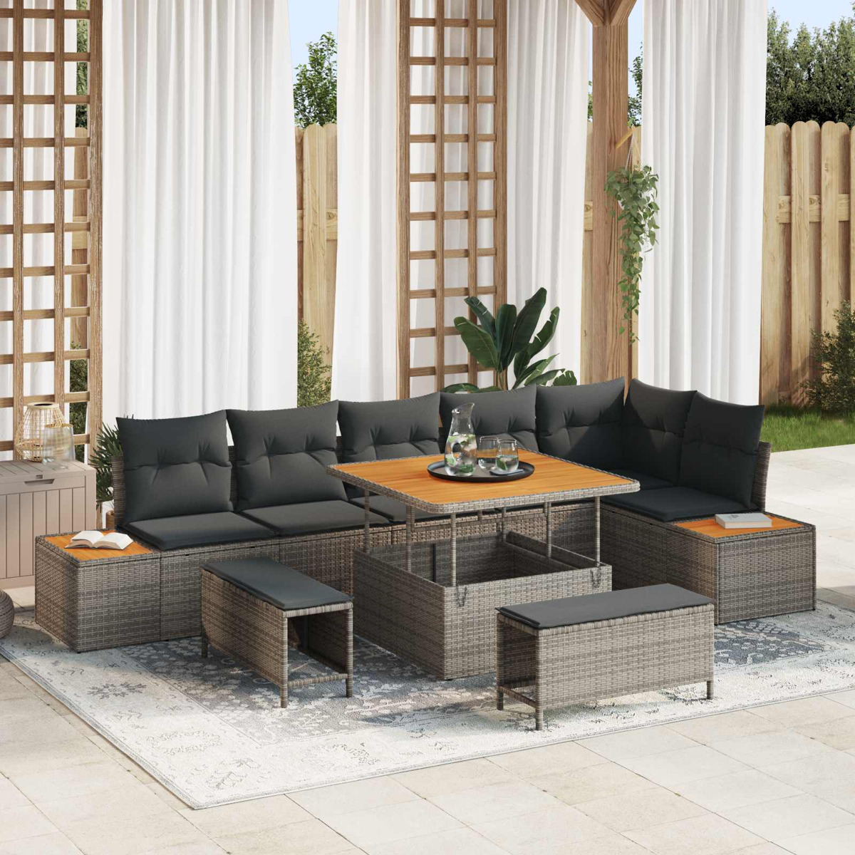 Ein graues Rattan-Loungeset mit Tisch, Kissen und Hockern auf einer Terrasse.