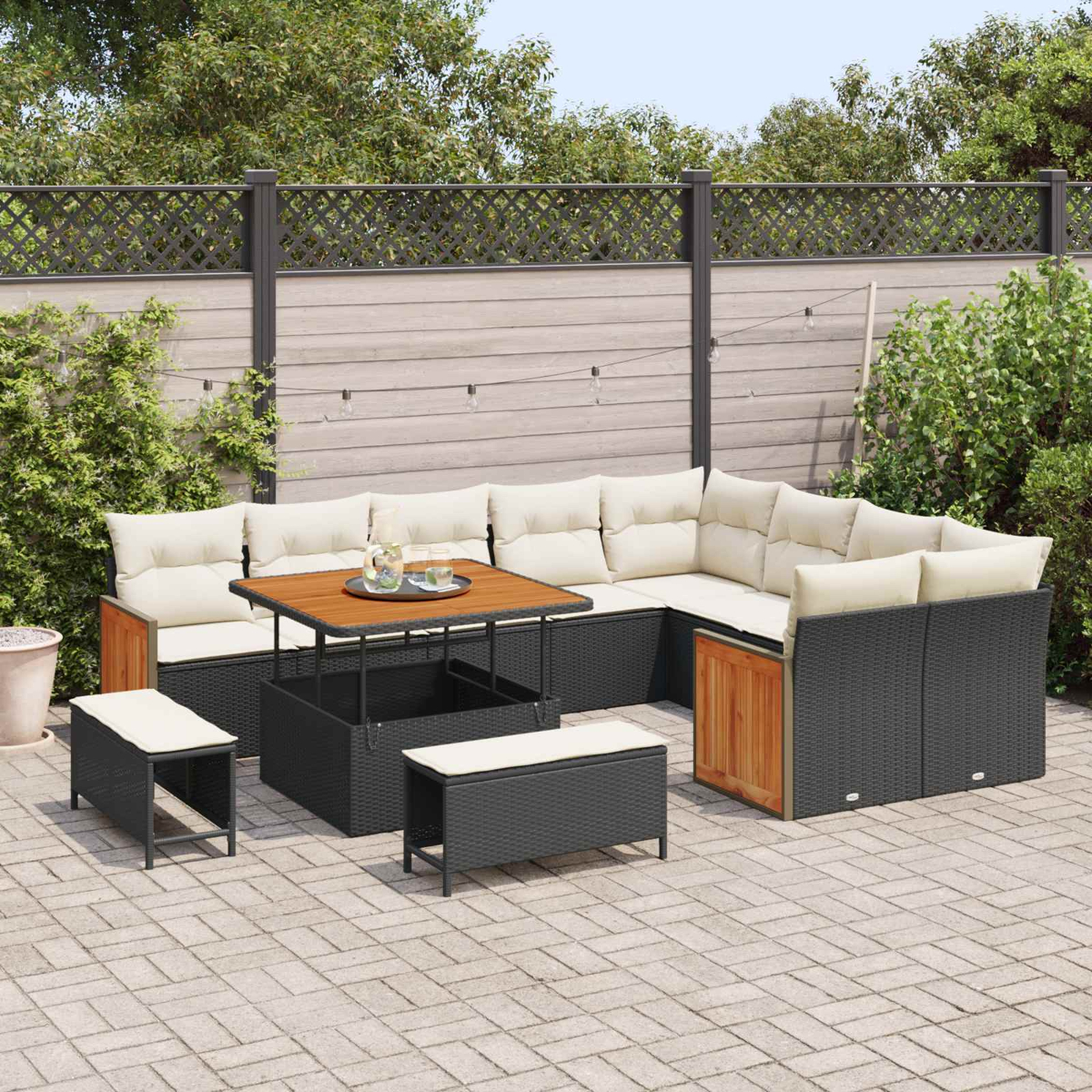 Ein dunkles Rattan-Sofa mit beigen Kissen und Holzakzenten auf einer gepflasterten Terrasse.